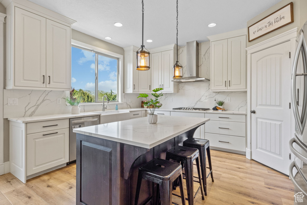 Kitchen with wall chimney exhaust hood, stainless steel appliances, white cabinets, light wood-style flooring, and recessed lighting