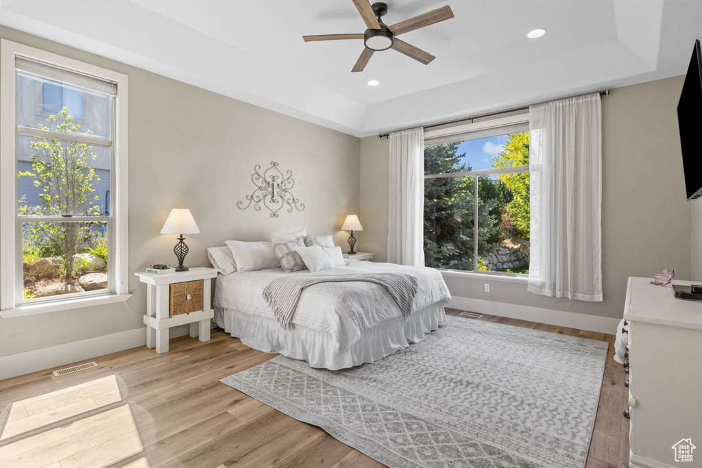 Bedroom with a tray ceiling, light wood finished floors, baseboards, recessed lighting, and a ceiling fan