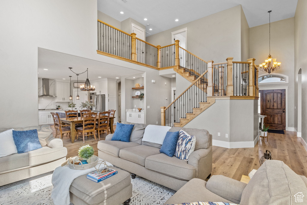 Living area featuring a chandelier, a towering ceiling, light wood-type flooring, stairway, and baseboards