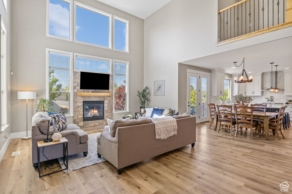 Living area featuring a towering ceiling, a stone fireplace, light wood-style floors, baseboards, and a chandelier