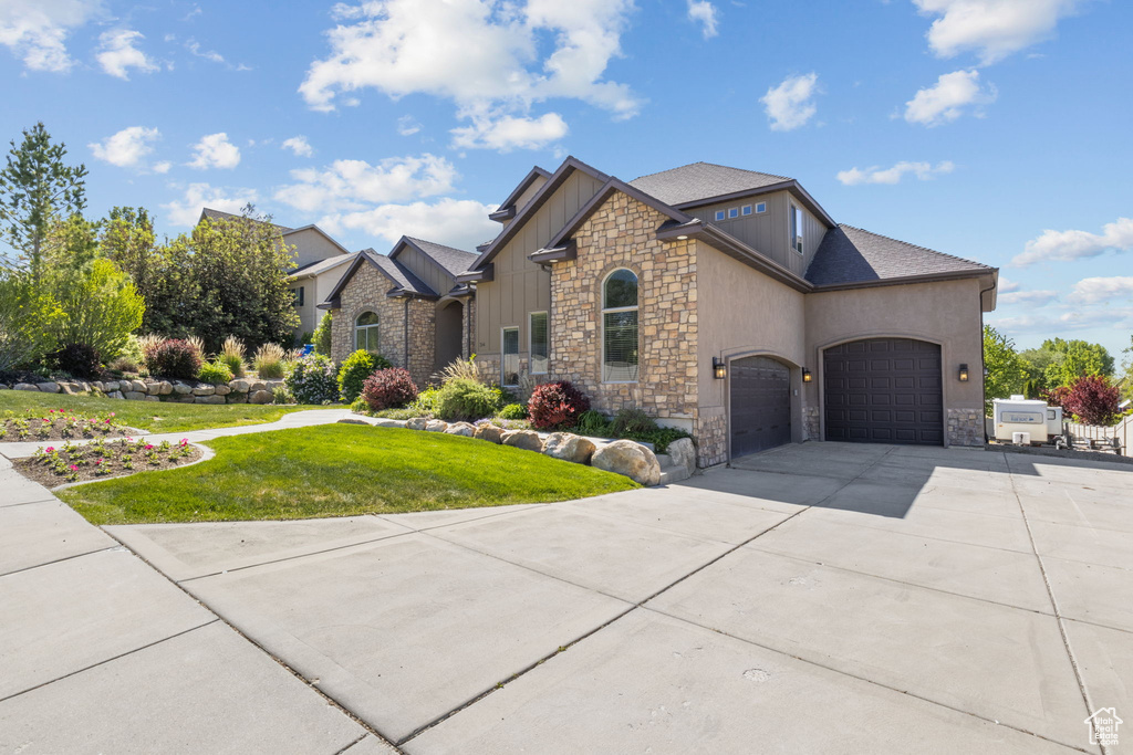 View of front of property featuring stone siding, an attached garage, a front yard, and concrete driveway