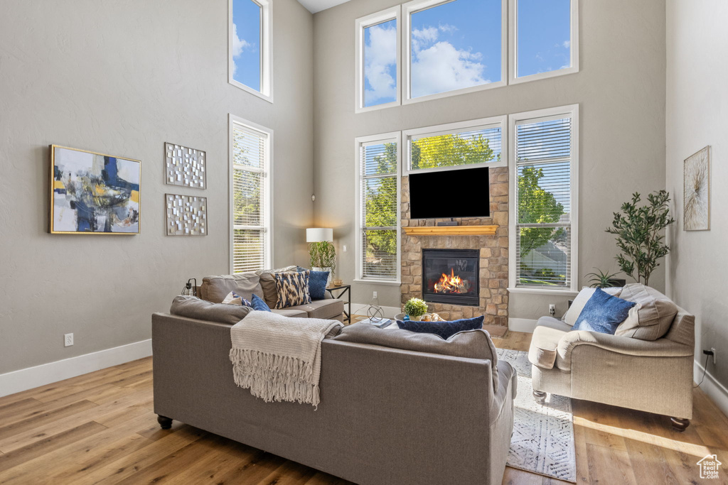 Living area with a high ceiling, wood finished floors, baseboards, plenty of natural light, and a stone fireplace