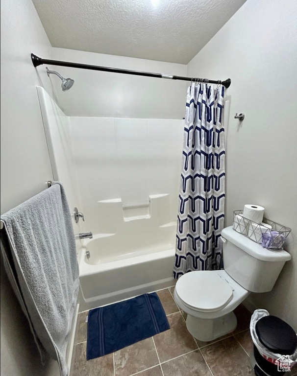 Bathroom with shower / tub combo with curtain, toilet, tile patterned floors, and a textured ceiling