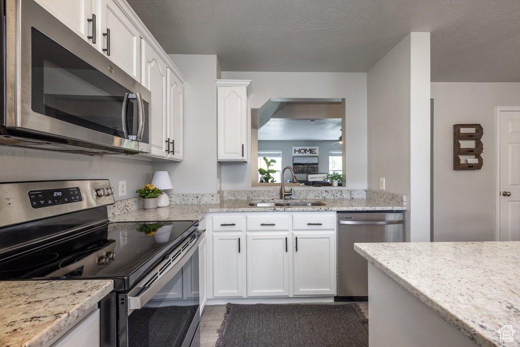 Kitchen featuring appliances with stainless steel finishes, a sink, white cabinets, and light stone counters