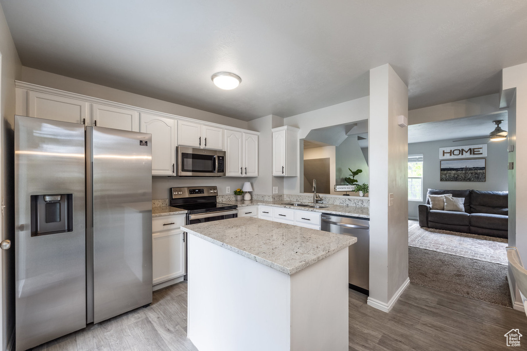 Kitchen featuring appliances with stainless steel finishes, wood finished floors, white cabinetry, and a kitchen island