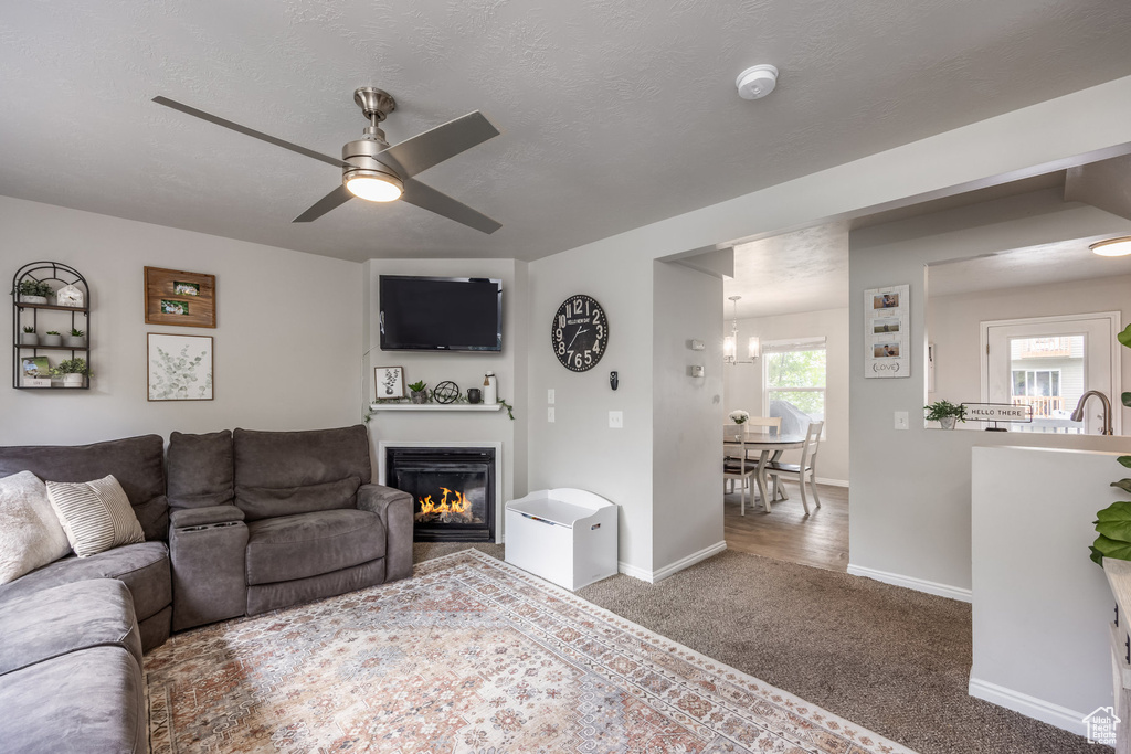 Living room with a glass covered fireplace, ceiling fan, baseboards, and carpet flooring