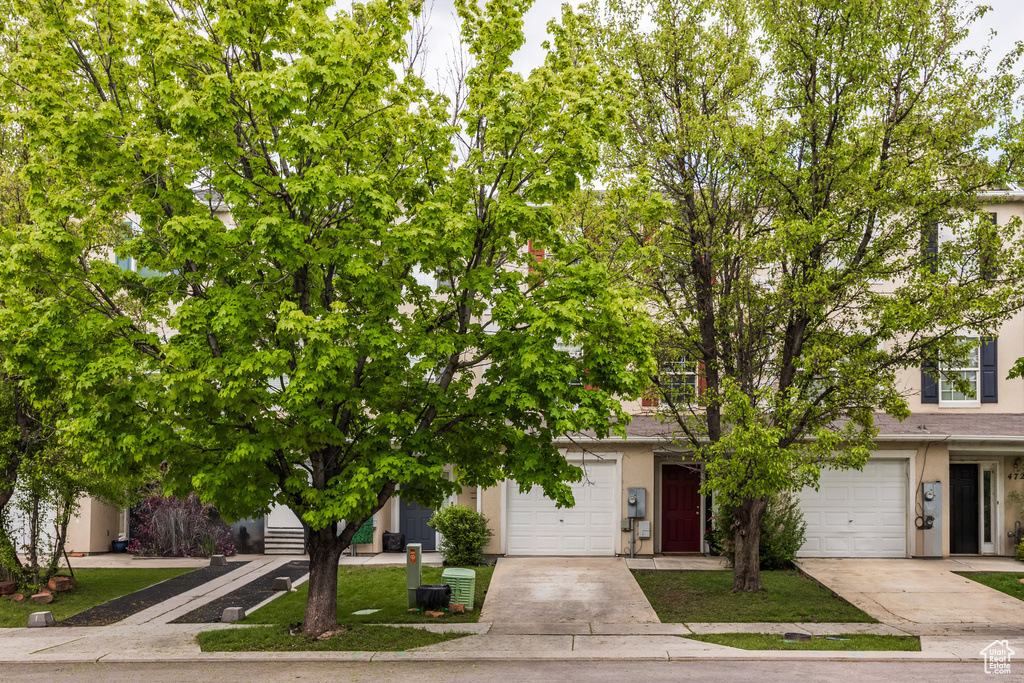 View of property hidden behind natural elements with stucco siding, driveway, and an attached garage