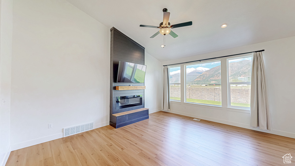 Unfurnished living room featuring a large fireplace, wood finished floors, lofted ceiling, ceiling fan, and baseboards