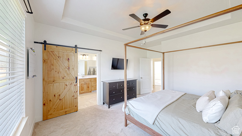 Bedroom with a barn door, light carpet, ensuite bath, and a ceiling fan