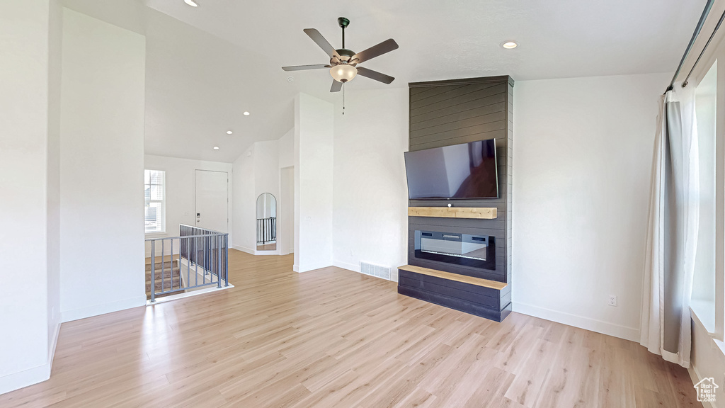 Unfurnished living room with lofted ceiling, wood finished floors, a ceiling fan, baseboards, and a large fireplace