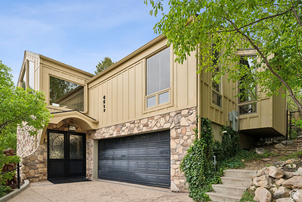 View of front of home featuring stone siding, french doors, a garage, board and batten siding, and driveway