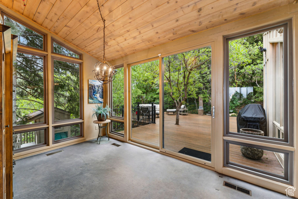 Unfurnished sunroom featuring healthy amount of natural light, vaulted ceiling, a chandelier, carpet, and wooden ceiling