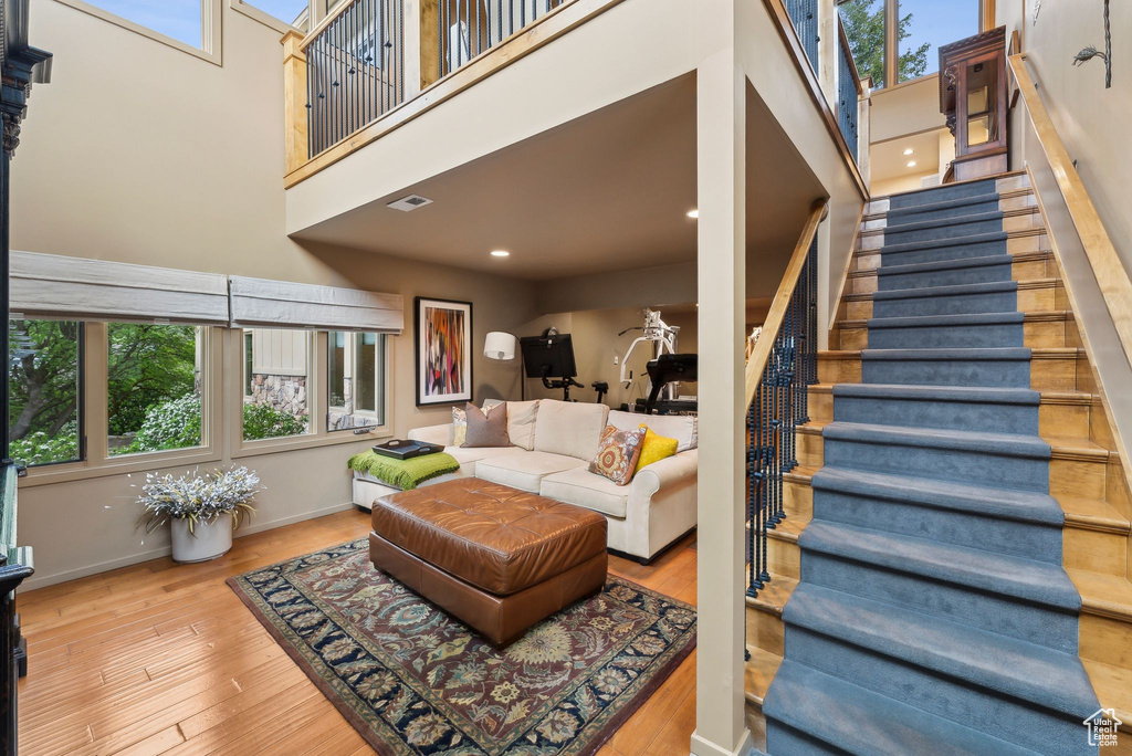 Living room featuring a towering ceiling, plenty of natural light, stairs, wood finished floors, and recessed lighting