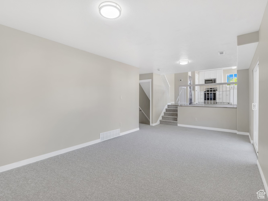 Unfurnished living room with light colored carpet, stairs, and baseboards