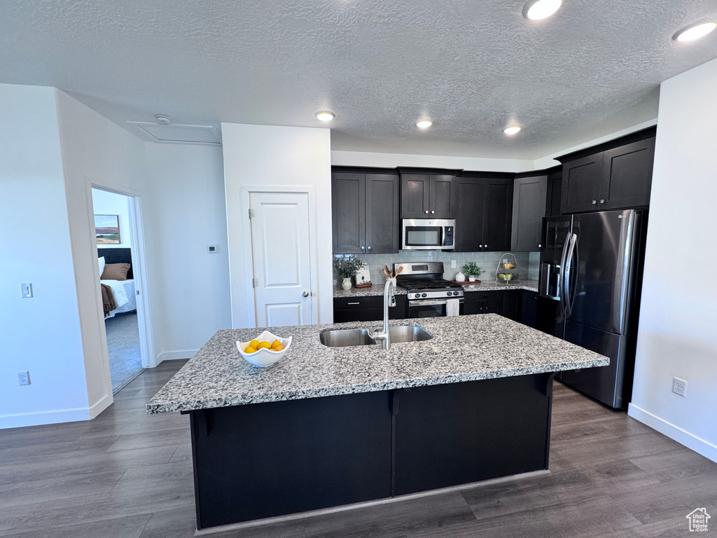 Kitchen featuring stainless steel appliances, a sink, baseboards, a textured ceiling, and decorative backsplash