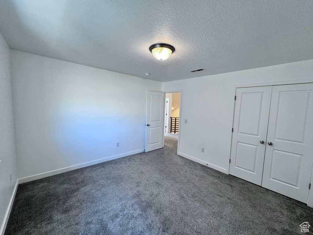 Unfurnished bedroom featuring dark colored carpet, baseboards, a textured ceiling, and a closet