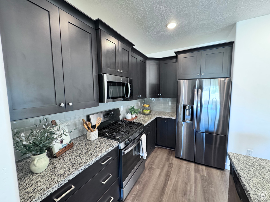 Kitchen featuring appliances with stainless steel finishes, light wood-style flooring, a textured ceiling, light stone countertops, and backsplash
