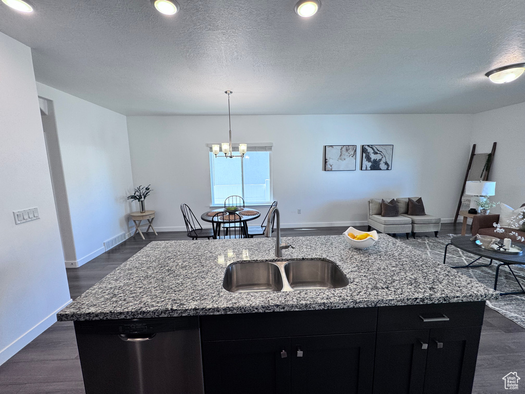 Kitchen with a sink, dishwasher, dark cabinets, open floor plan, and a kitchen island with sink