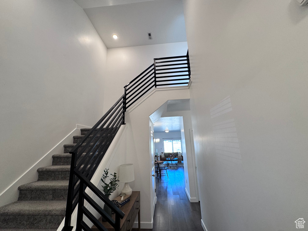 Stairs with wood finished floors, recessed lighting, baseboards, and a towering ceiling