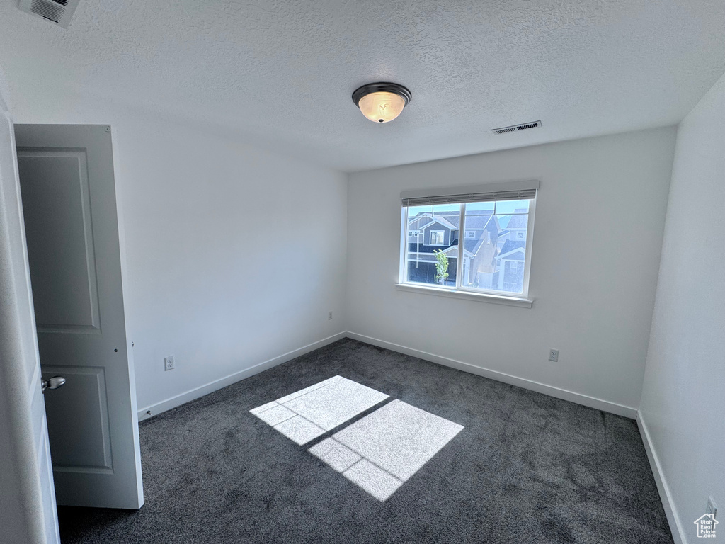 Spare room with dark carpet, a textured ceiling, and baseboards