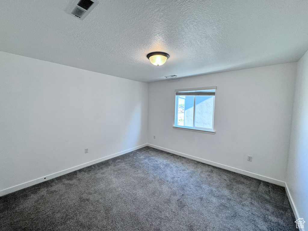Spare room with dark carpet, baseboards, and a textured ceiling