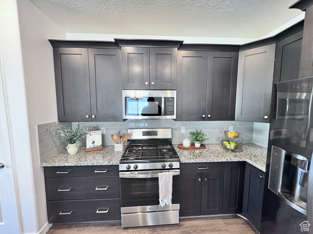Kitchen featuring appliances with stainless steel finishes, light wood finished floors, tasteful backsplash, light stone countertops, and a textured ceiling