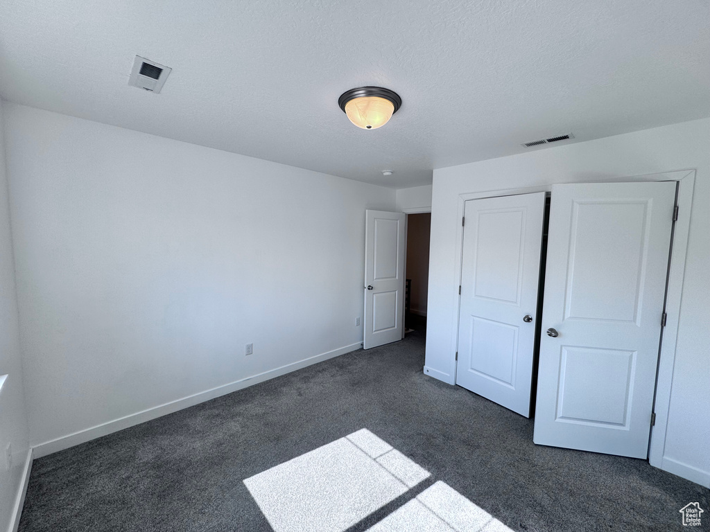 Unfurnished bedroom featuring dark colored carpet, baseboards, and a closet