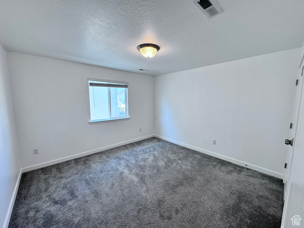 Unfurnished room featuring dark colored carpet, baseboards, and a textured ceiling