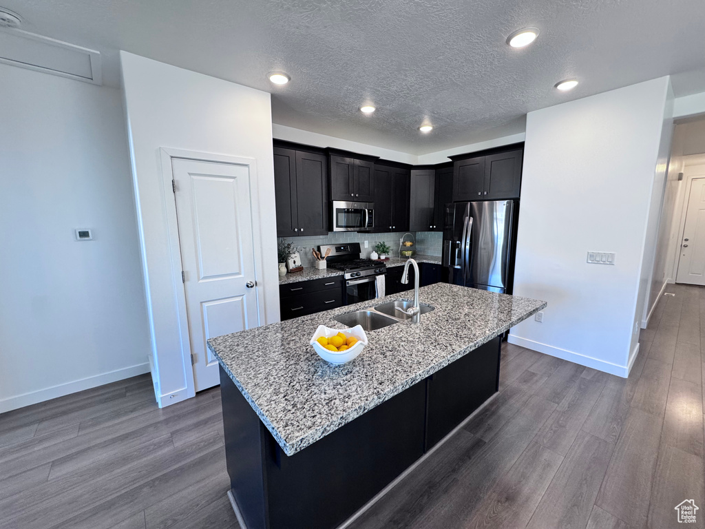 Kitchen featuring appliances with stainless steel finishes, a sink, dark wood-type flooring, baseboards, and a textured ceiling