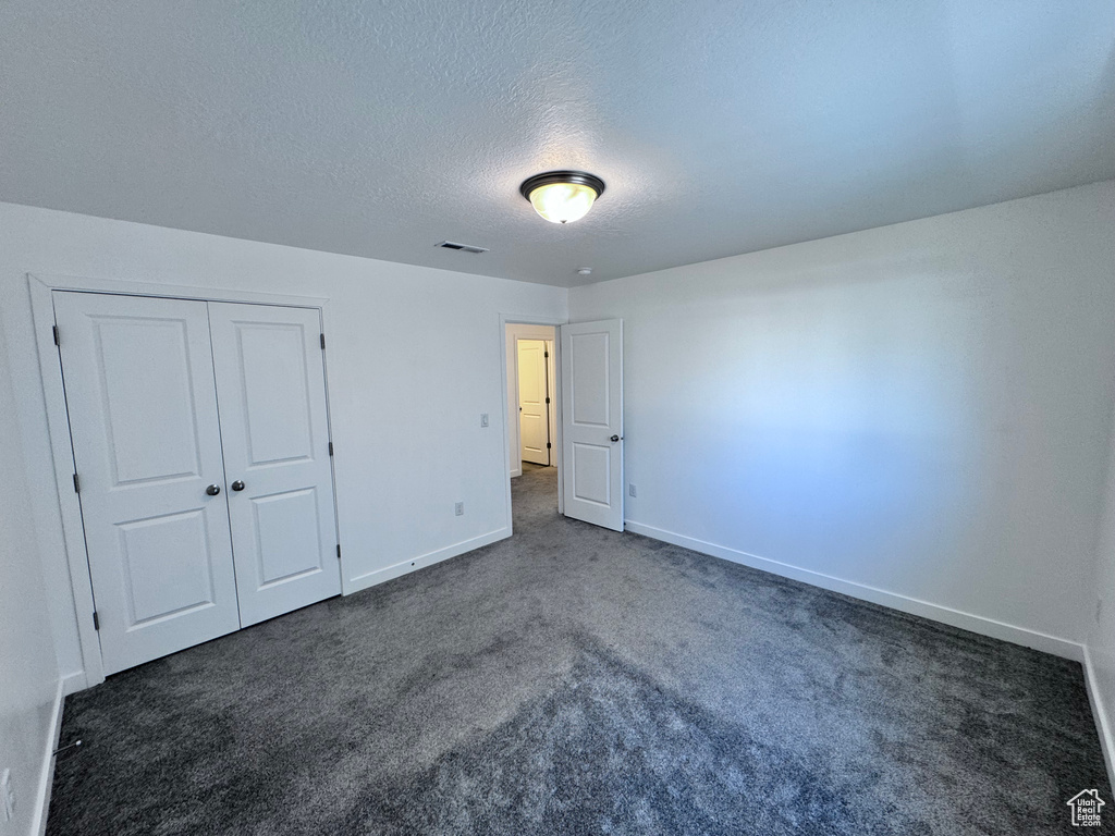 Unfurnished bedroom featuring dark carpet, baseboards, a textured ceiling, and a closet