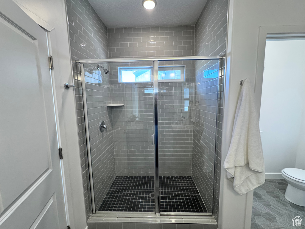 Bathroom featuring a stall shower, toilet, a textured ceiling, and baseboards