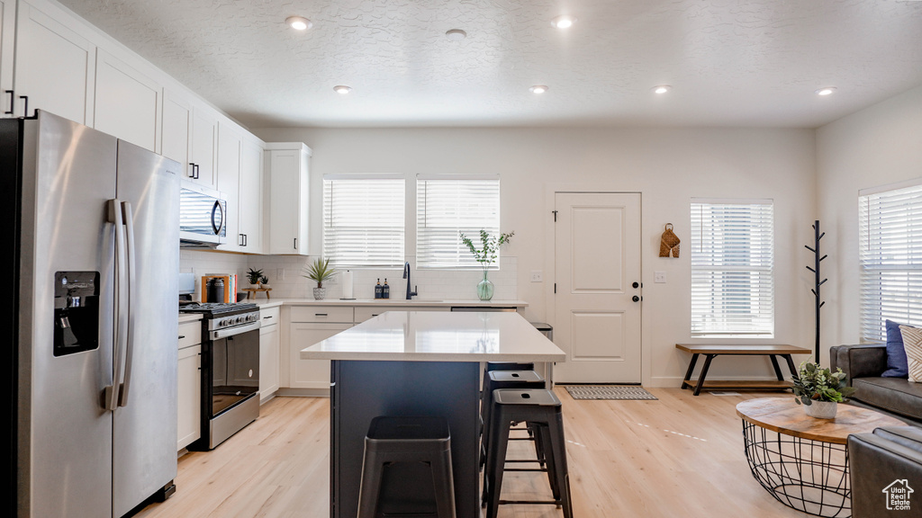 Kitchen with appliances with stainless steel finishes, a sink, light countertops, light wood-style floors, and a breakfast bar