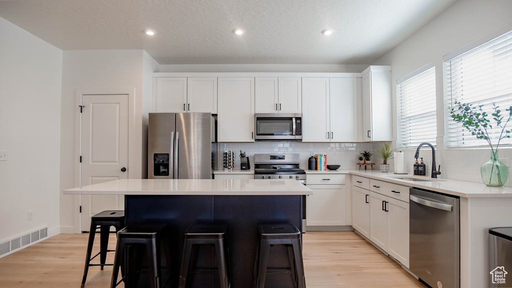 Kitchen with appliances with stainless steel finishes, a sink, a kitchen breakfast bar, a center island, and decorative backsplash