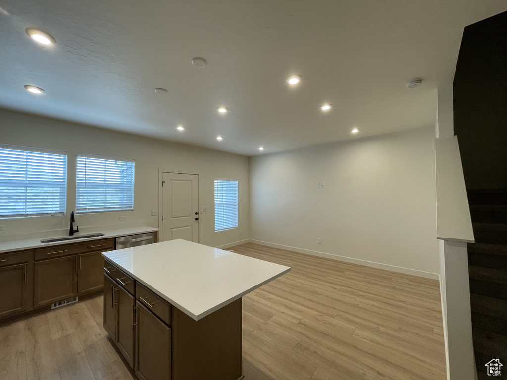 Kitchen with a sink, light wood-style flooring, light countertops, a kitchen island, and plenty of natural light