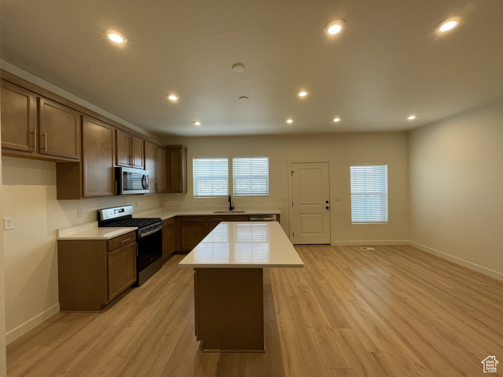 Kitchen with appliances with stainless steel finishes, a sink, light countertops, a center island, and baseboards