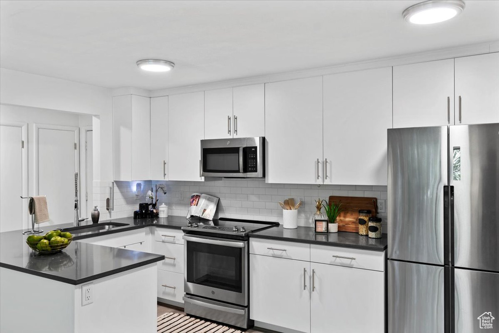 Kitchen featuring appliances with stainless steel finishes, dark countertops, white cabinetry, and backsplash