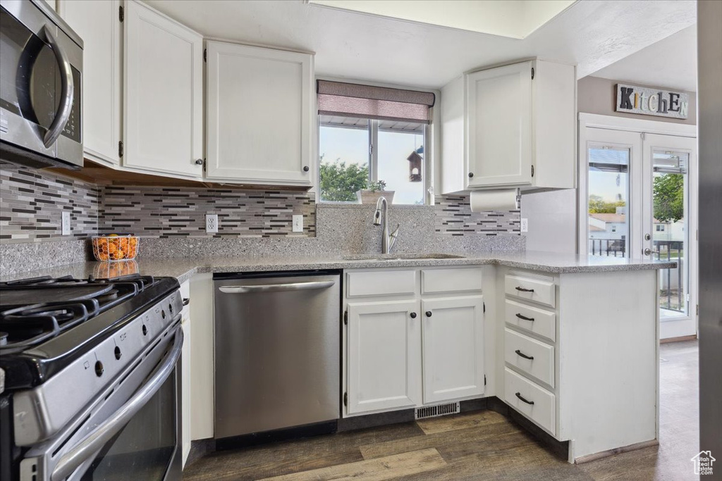 Kitchen with appliances with stainless steel finishes, a sink, white cabinetry, and dark wood-style floors