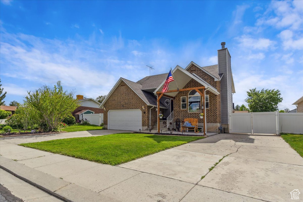 Traditional-style home featuring concrete driveway, a gate, brick siding, a chimney, and an attached garage