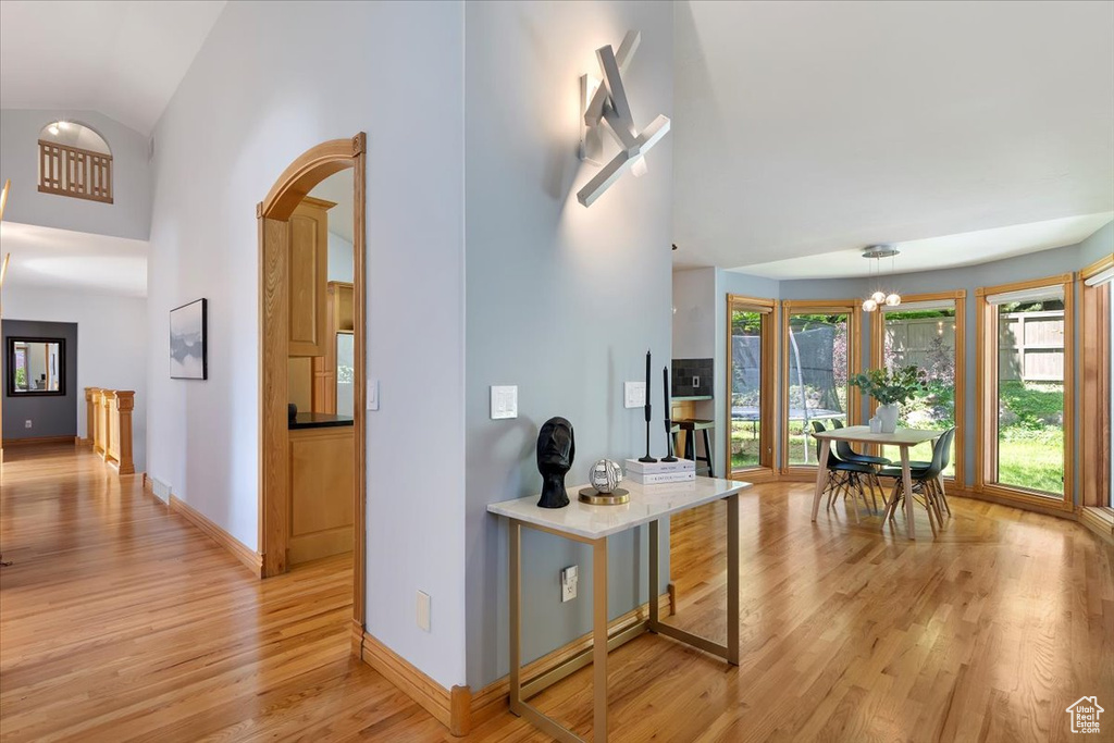 Corridor featuring light wood finished floors, baseboards, a chandelier, high vaulted ceiling, and arched walkways