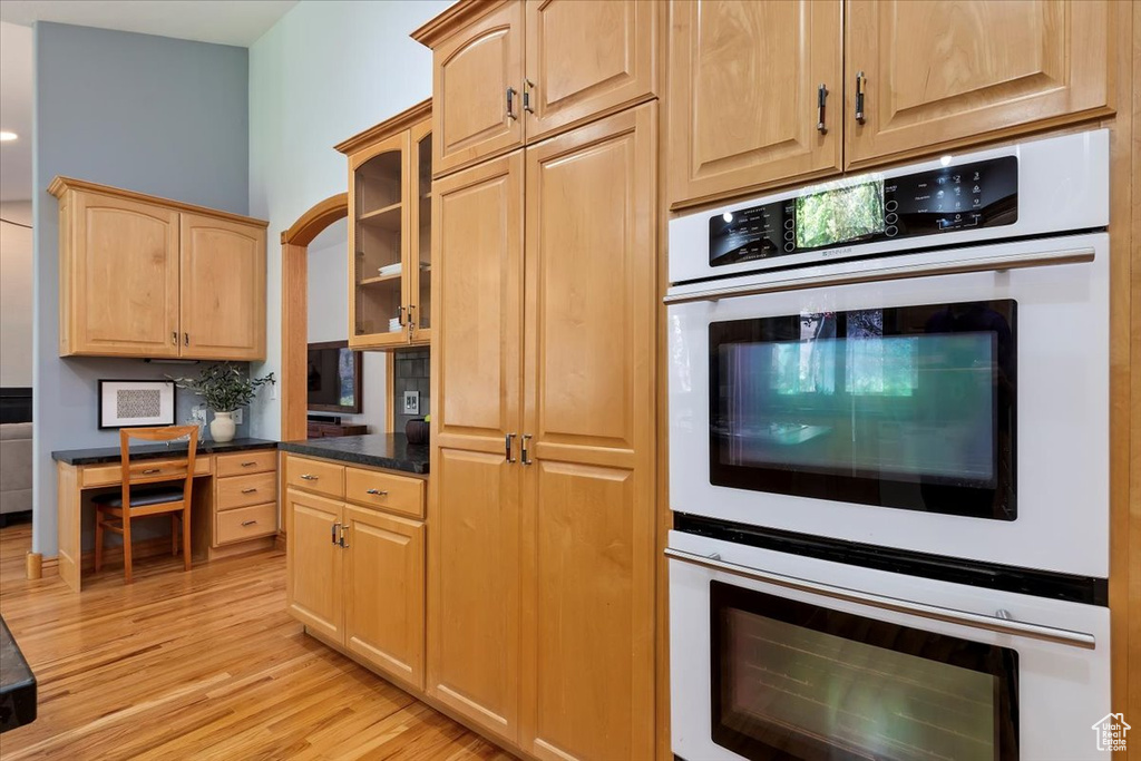 Kitchen featuring double oven, light wood finished floors, light brown cabinets, and glass insert cabinets