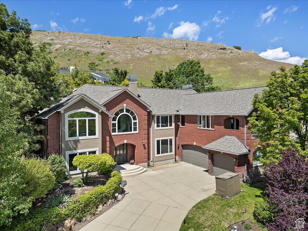 View of front facade with concrete driveway, a chimney, a garage, brick siding, and a mountain view