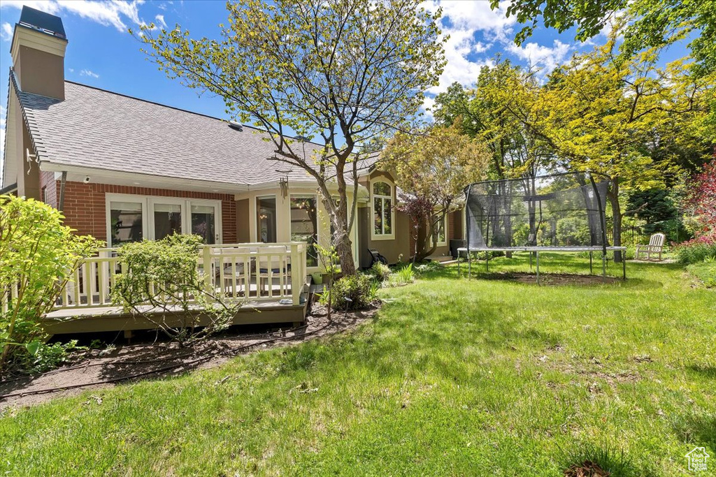 View of grassy yard featuring a trampoline and a wooden deck