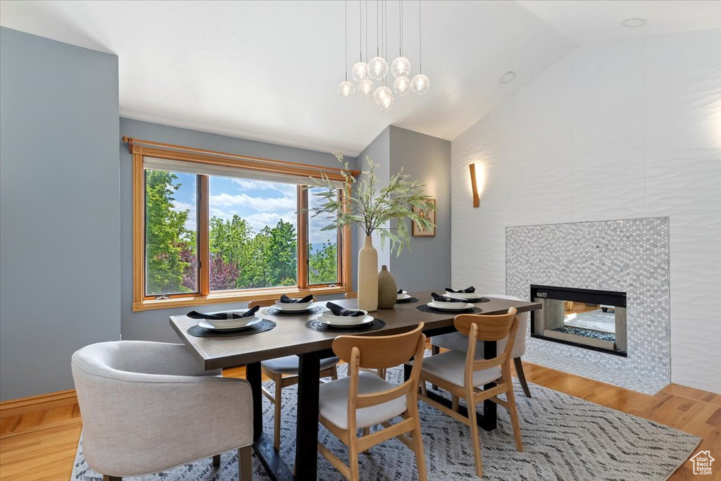 Dining space featuring vaulted ceiling, wood finished floors, a fireplace, and a chandelier