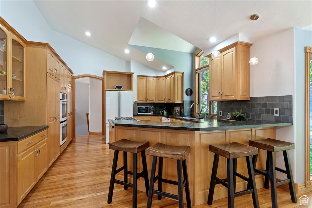 Kitchen featuring a peninsula, a sink, light wood-style flooring, backsplash, and lofted ceiling