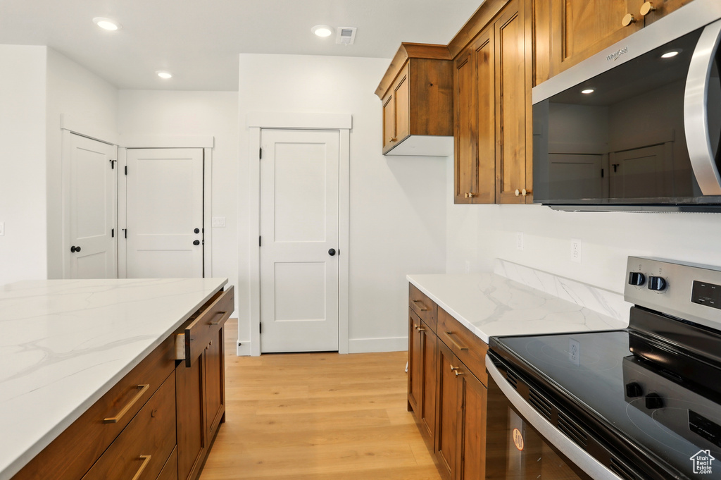 Kitchen with stainless steel appliances, brown cabinetry, light wood finished floors, light stone counters, and recessed lighting