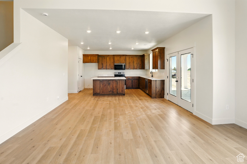 Kitchen with stainless steel appliances, light wood-style flooring, light countertops, baseboards, and a center island