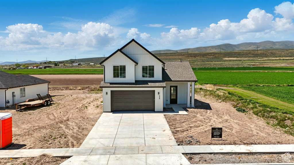 Modern farmhouse featuring a mountain view, driveway, an attached garage, and a view of rural / pastoral area