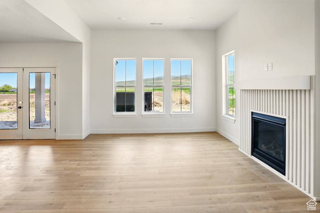 Unfurnished living room featuring baseboards, light wood finished floors, a glass covered fireplace, and french doors