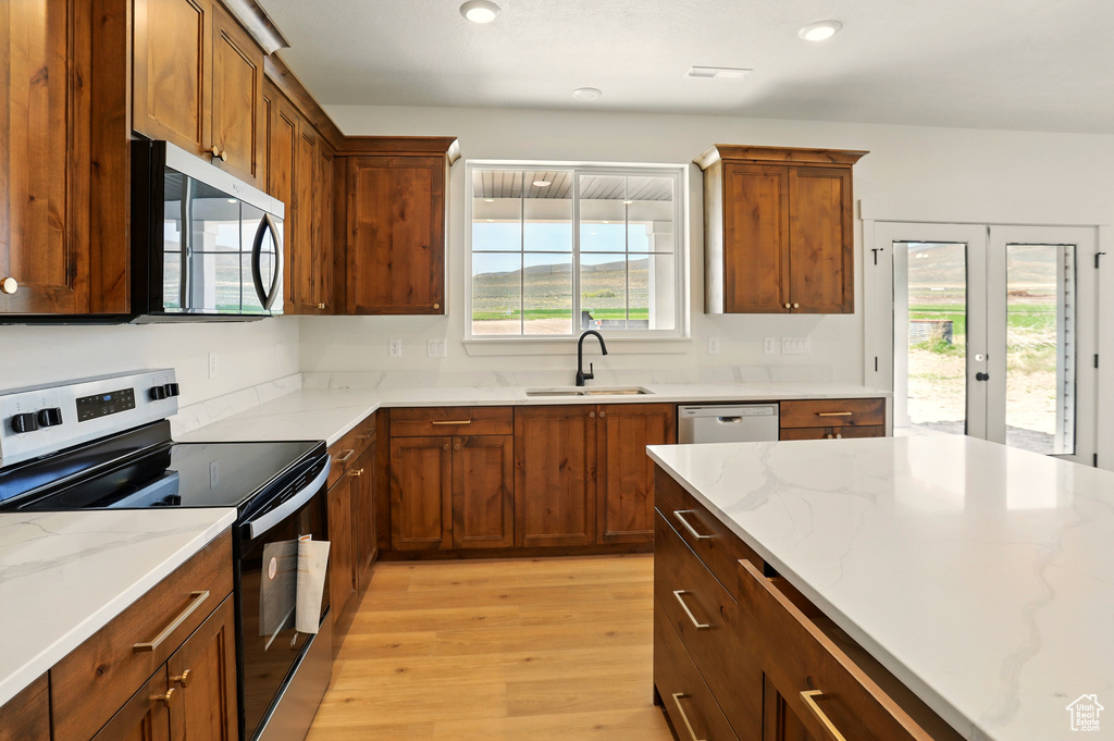 Kitchen featuring appliances with stainless steel finishes, light wood-style flooring, a sink, light stone counters, and french doors