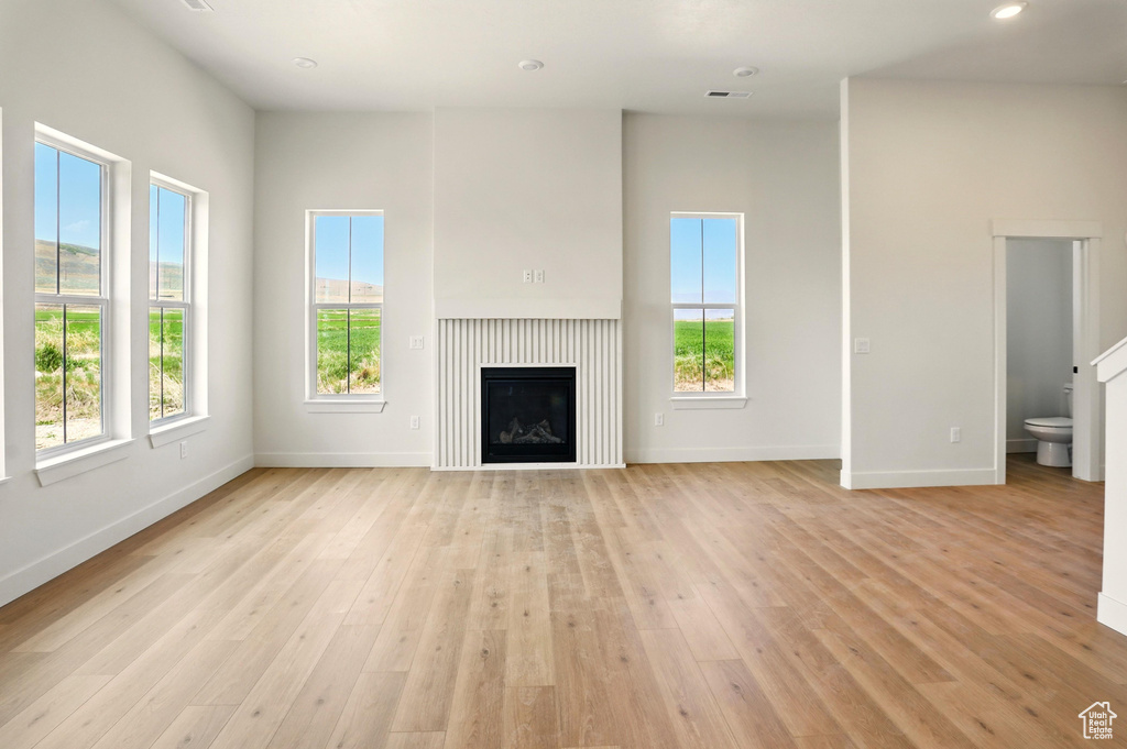 Unfurnished living room with plenty of natural light, baseboards, light wood finished floors, a glass covered fireplace, and recessed lighting